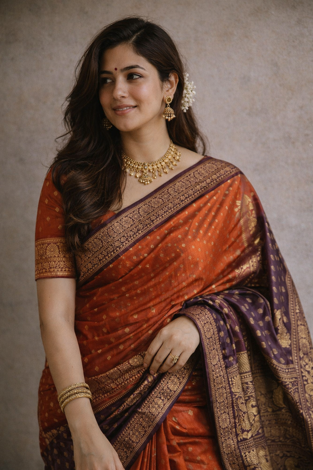Woman wearing a traditional saree with gold jewelry against a neutral background