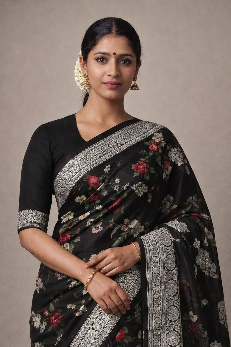 Woman wearing a black saree with floral patterns and silver border against a plain background